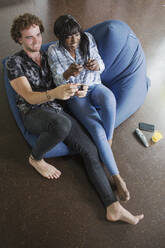 Young multiethnic couple playing video game in beanbag chair - HOXF05019