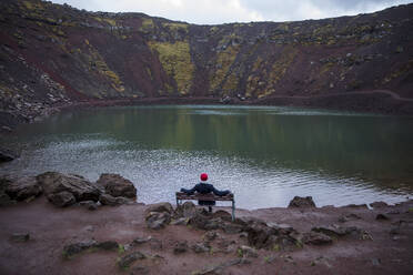 Wanderer auf einer Bank mit Blick auf einen See in den Bergen - JOHF08754