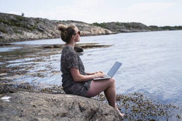 Woman using laptop at sea - JOHF08804