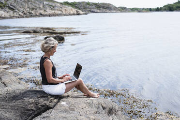 Woman using laptop at sea - JOHF08806