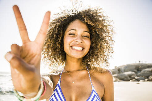 Portait of happy young woman making victory sign on the beach - SDAHF00500