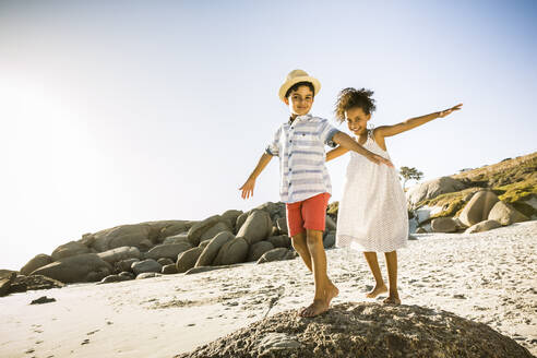 Glücklicher Junge und Mädchen balancieren auf einem Felsen am Strand - SDAHF00508