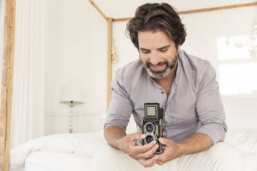 Bärtiger Mann auf dem Bett sitzend mit altmodischer Kamera - SDAHF00559