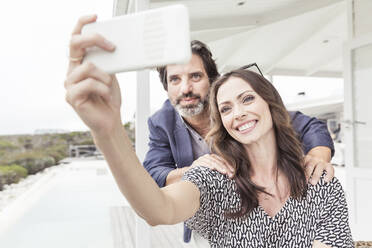 Smiling couple taking a selfie at a vacation home - SDAHF00573