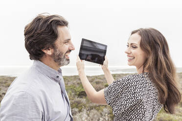 Happy man looking at wife holding tablet at the coast - SDAHF00574