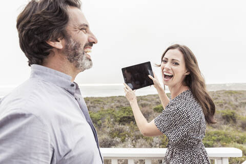 Glücklicher Mann mit Frau, die ein Tablet an der Küste hält, lizenzfreies Stockfoto