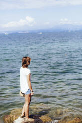 Young woman standing at the lakeside, Lake Garda, Italy - GIOF08002