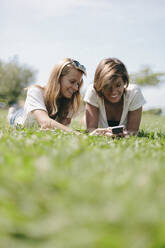 Two smiling female friends lying on a meadow sharing cell phone - GIOF08003