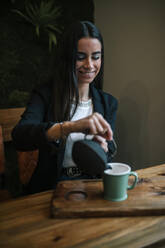 Porträt einer jungen Frau in einem Café, die Tee in eine Tasse gießt - GRCF00162