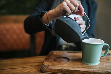 Crop-Ansicht einer Frau in einem Café, die Tee in eine Tasse gießt - GRCF00163