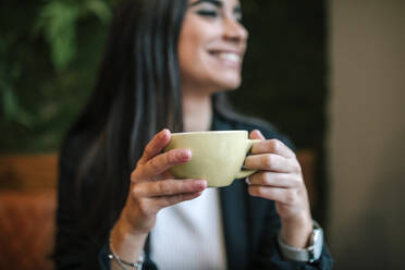 Crop view of happy woman in a coffee shop holding cup - GRCF00164