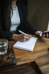 Crop-Ansicht einer Frau mit Smartphone in einem Café, die sich Notizen macht - GRCF00165