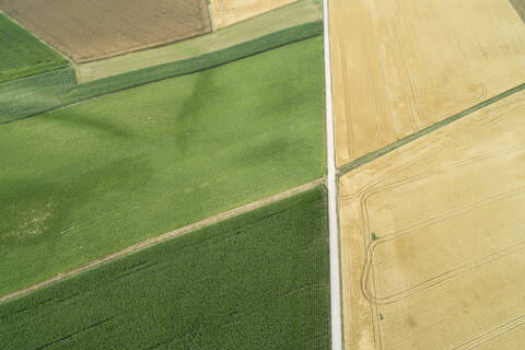 Deutschland, Bayern, Drohnenansicht einer Landstraße, die sich zwischen grünen und gelben Feldern im Sommer erstreckt, lizenzfreies Stockfoto