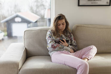 Teenager-Mädchen auf Sofa mit Handy - JOHF08900