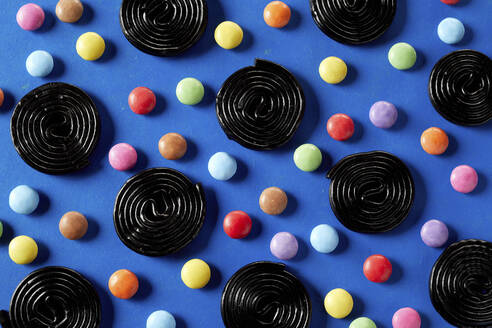 Spirals of liquorice interspersed with colorful sugar-coated chocolate candy on blue background - DREF00048