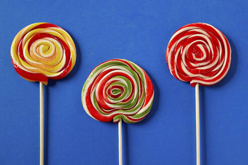 Three colorful spiral lollipops on a blue background arranged in a row - DREF00050