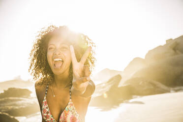 Portait of carefree young woman making victory sign on the beach - SDAHF00599