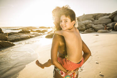 Mutter trägt ihren lächelnden Sohn Huckepack am Strand - SDAHF00612