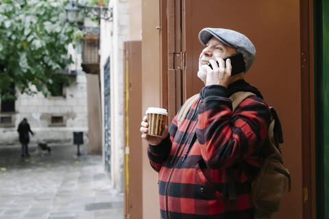 Älterer Mann am Telefon mit Coffee to go und Rucksack in der Stadt, Barcelona, Spanien, lizenzfreies Stockfoto