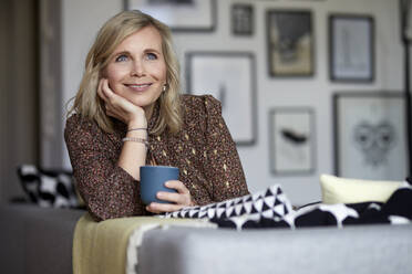 Smiling blond woman relaxing at home sitting on couch - RBF07045