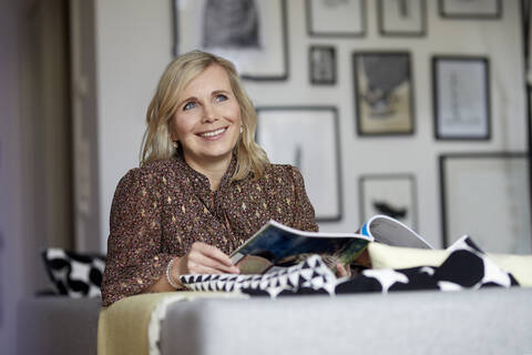 Lächelnde blonde Frau entspannt zu Hause auf der Couch sitzend, lizenzfreies Stockfoto