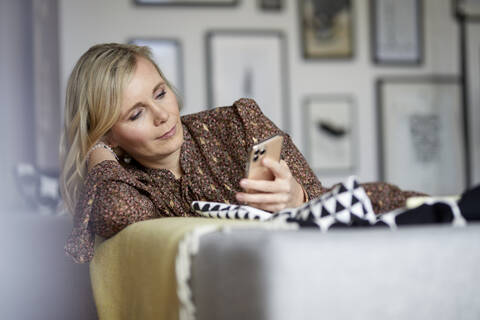 Blonde Frau benutzt Mobiltelefon zu Hause, lizenzfreies Stockfoto