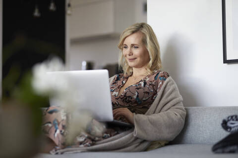 Blond woman using laptop on couch at home stock photo