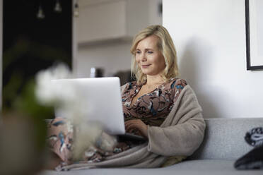 Blonde Frau mit Laptop auf der Couch zu Hause - RBF07058