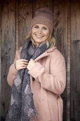 Porträt einer lächelnden Frau in Winterkleidung an einer Holzwand - RBF07067