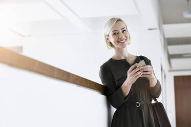 Portrait of smiling businesswoman with mobile phone and handbag - BMOF00179