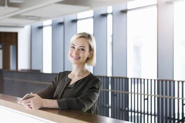 Portrait of happy businesswoman with mobile phone leaning on railing - BMOF00181