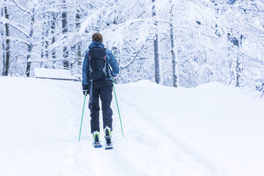 Germany, Bavaria, Reit im Winkl, Female backpacker skiing in winter forest - MMAF01257