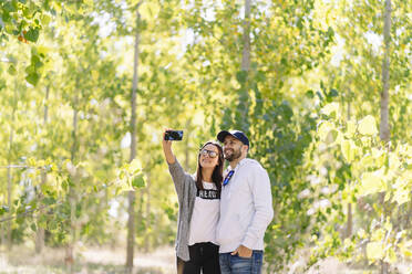 Lächelndes Paar macht ein Selfie in einem Park - DGOF00429