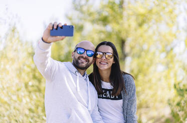 Paar mit Sonnenbrille und Selfie in einem Park - DGOF00436