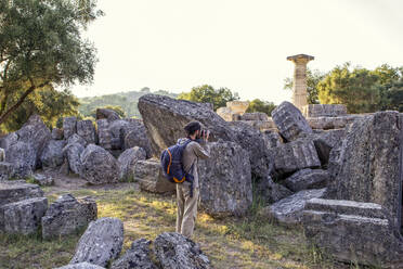 Griechenland, Olympia, Männlicher Tourist fotografiert Ruinen des antiken Zeus-Tempels bei Sonnenuntergang - MAMF01186