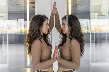 Woman touching mirror images of herself on a glasspane - DLTSF00528