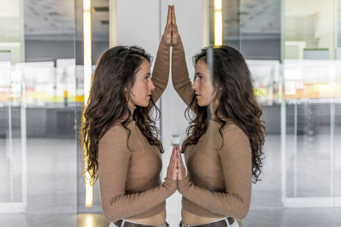 Frau berührt Spiegelbilder von sich selbst auf einer Glasscheibe - DLTSF00528
