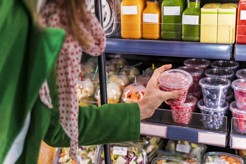 Woman taking packaged berries from cooling shelf in organic store - DLTSF00533