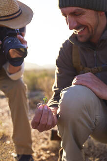 Lächelnder Safari-Reiseleiter erklärt einem Mann mit Digitalkamera eine Pflanze - CAIF23768