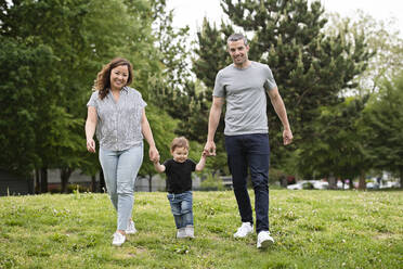 Portrait happy young family walking in park grass - CAIF23797