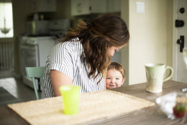 Mother and cute toddler daughter at kitchen table - CAIF23803