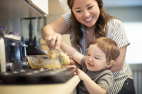 Glückliche Mutter und Kleinkind Tochter backen Muffins in der Küche - CAIF23807