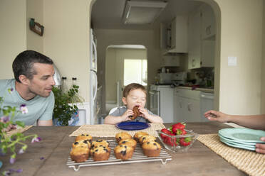 Vater beobachtet süßes Kleinkind Tochter essen Muffin am Küchentisch - CAIF23808