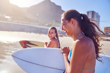 Glückliche junge Freundinnen mit Surfbrettern am sonnigen Strand - CAIF23821