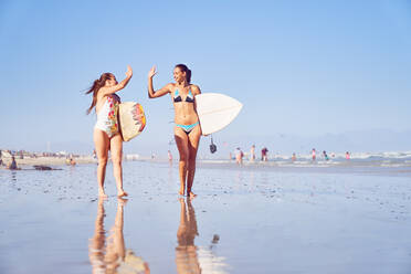 Glückliche junge Surferinnen, die sich am sonnigen Strand die Hände reichen - CAIF23842