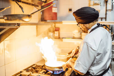 Indischer Koch flambiert Essen in Restaurantküche - OCMF01034