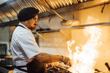 Indian chef flambing food in restaurant kitchen - OCMF01037