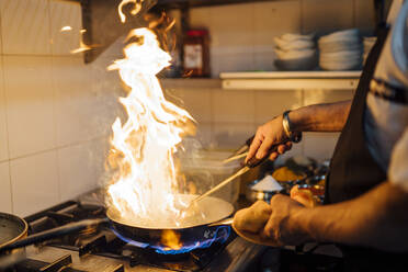 Indian chef flambing food in restaurant kitchen, close up - OCMF01038