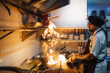 Indian chef flambing food in restaurant kitchen - OCMF01040