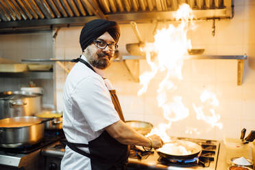 Indian chef flambing food in restaurant kitchen - OCMF01041